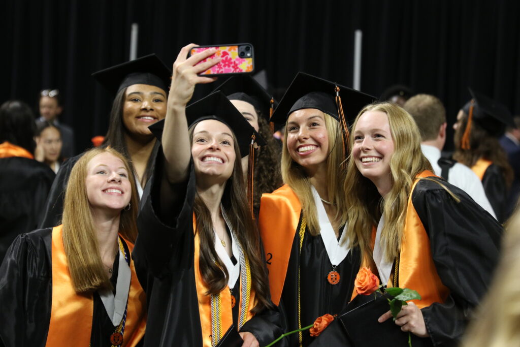 Students in graduation regalia take a selfie together on a cell phone